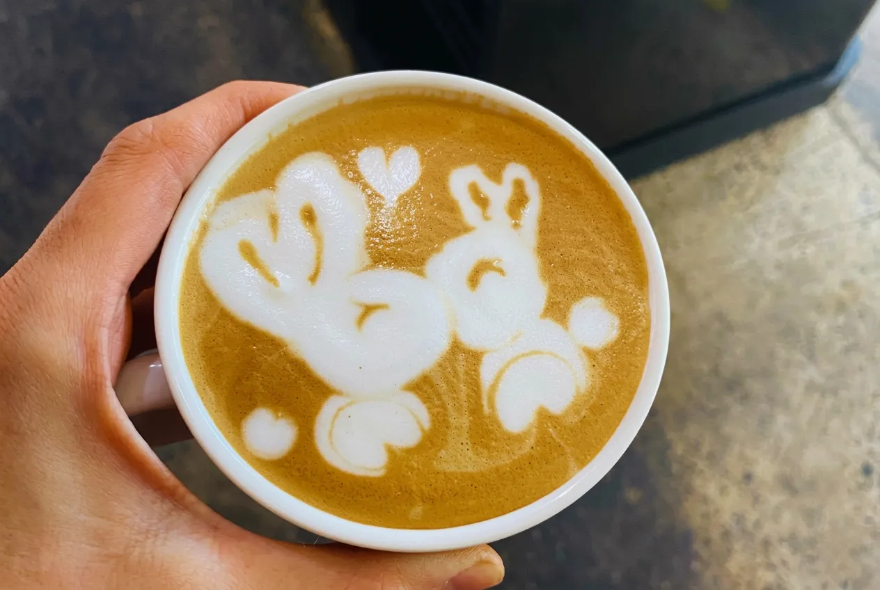 Barista-made latte held in hand, with detailed rabbit latte art poured in steamed milk